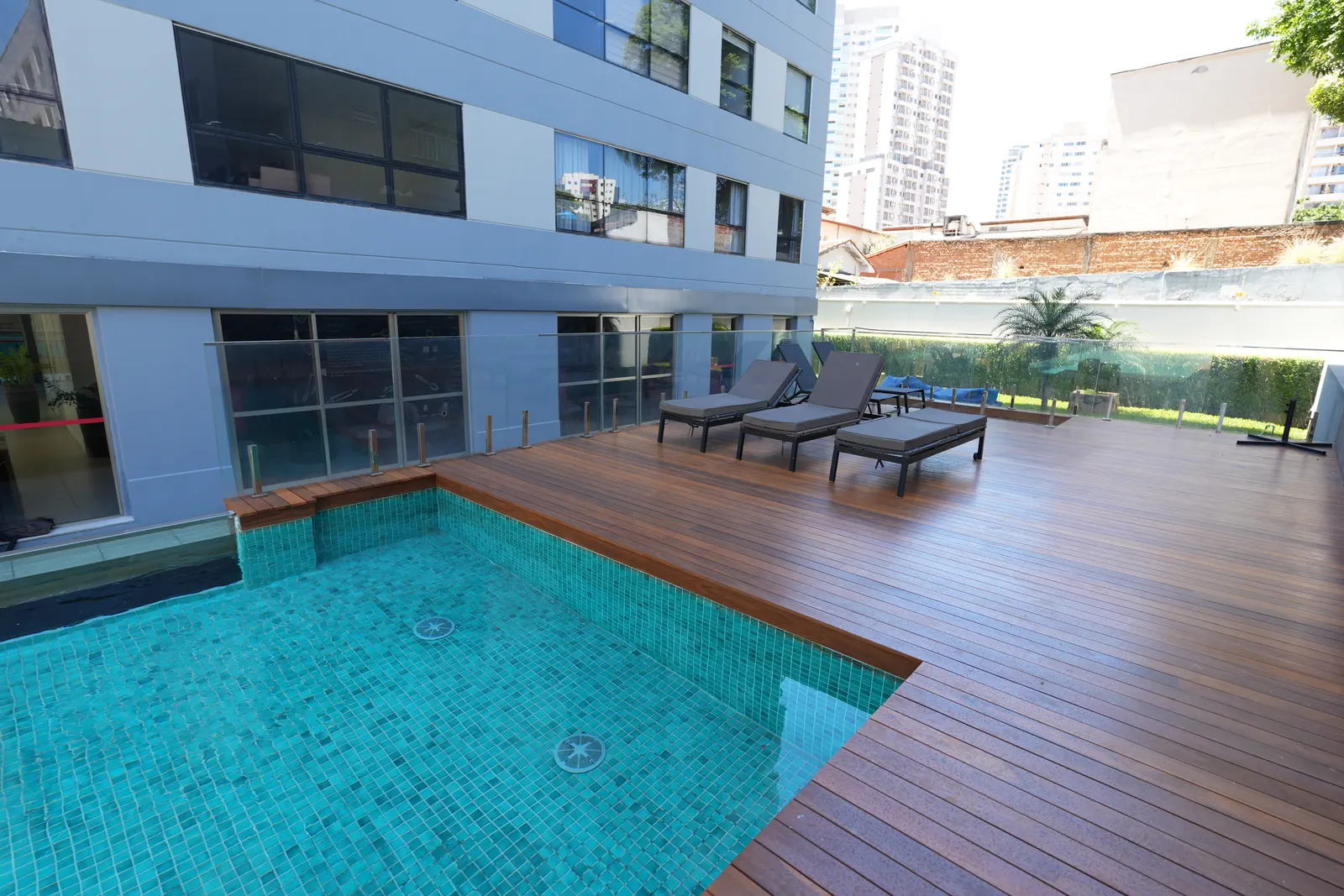 Deck de madeira em volta da piscina do MaxHaus Brooklin, com espreguiçadeiras e prédio ao fundo